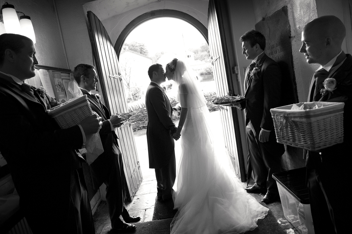 Bride-groom-kissing-doorway-st Illtud's-church=wedding-photographer